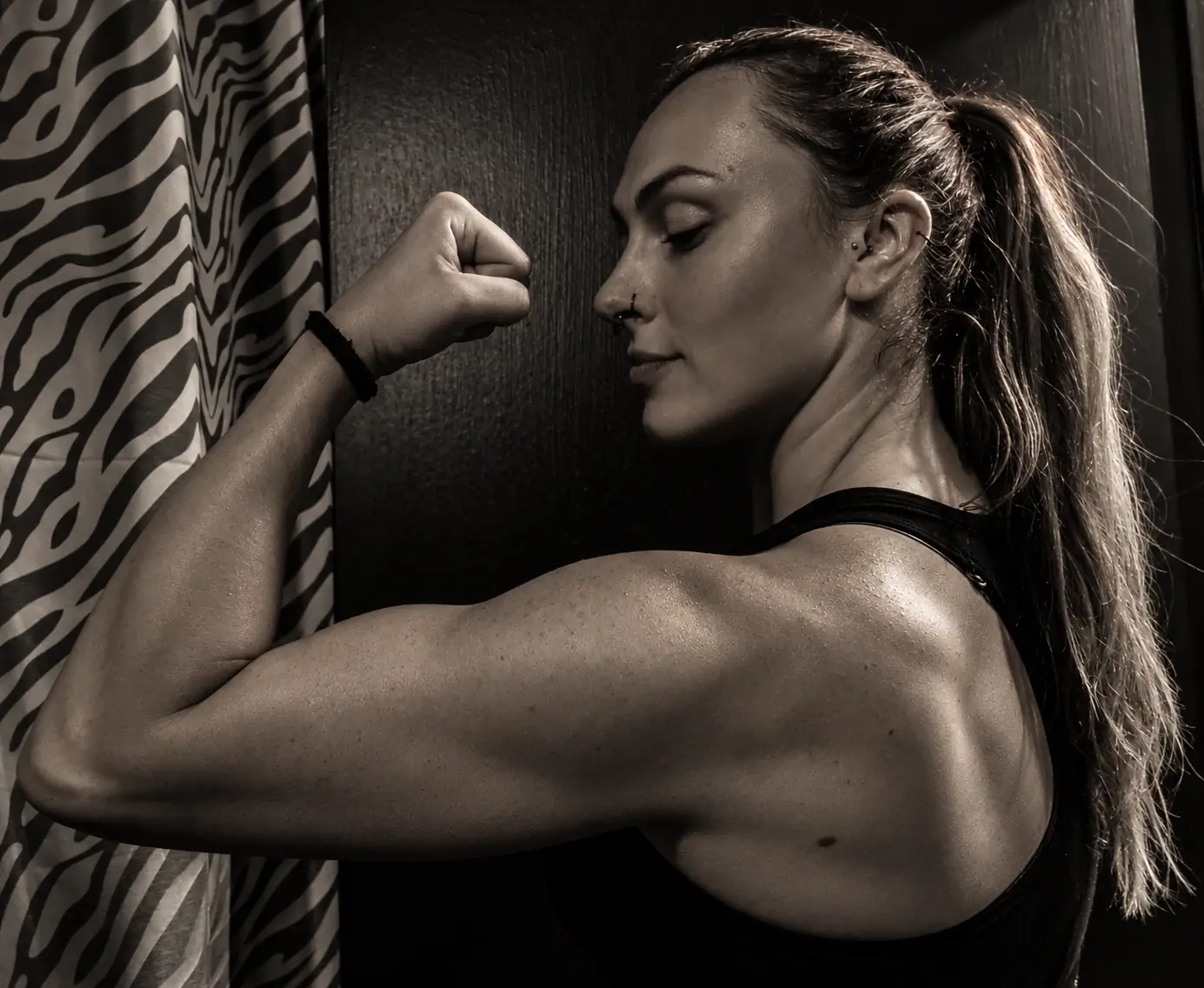 Portrait noir et blanc d’une femme en tenue sportive montrant son dos et son bras musclé.