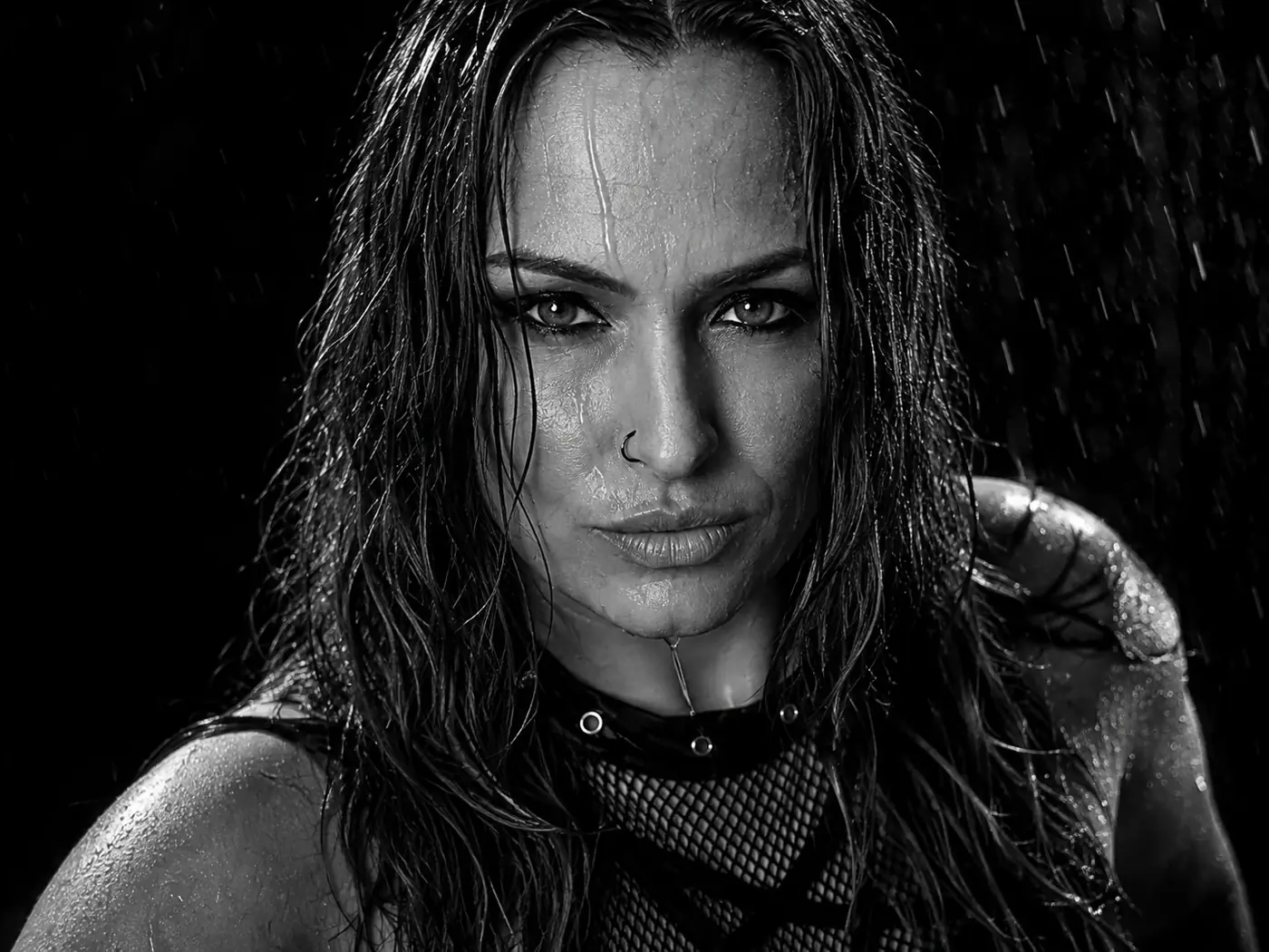 Portrait noir et blanc très contrasté d’une femme sous la pluie avec haut résille et expression intense.